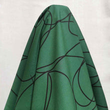 Load image into Gallery viewer, Klee is a stunning pure cotton with continuous, large scale, line drawings. Black on an emerald green background, available at Minerva's Bower. Fabric is draped over roll