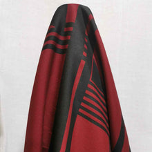 Load image into Gallery viewer, Metropolis is a dramatic, large scale graphic print. Pure cotton, with black on a claret red background, available at Minerva's Bower. Fabric is draped across roll