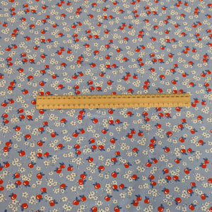 Flat lay of fabric with red apples and white flowers on a blue background in a vintage style, for sale at Minerva's Bower with a ruler included for scale