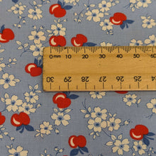 Load image into Gallery viewer, Close up of fabric with red apples and white flowers on a blue background in a vintage style, for sale at Minerva&#39;s Bower with a ruler included for scale