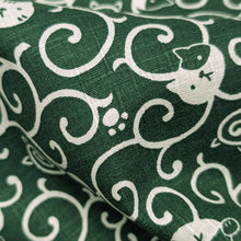 Load image into Gallery viewer, Pattern of white cats and swirls on a green cotton dobby background. Made in Japan. Available at Minerva's Bower. Fabric draped to show how it handles