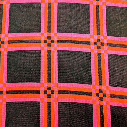 Flat lay of triple gauze Fabric with a checkered pattern of pink, orange, and black on a black background. Available at Minerva's Bower