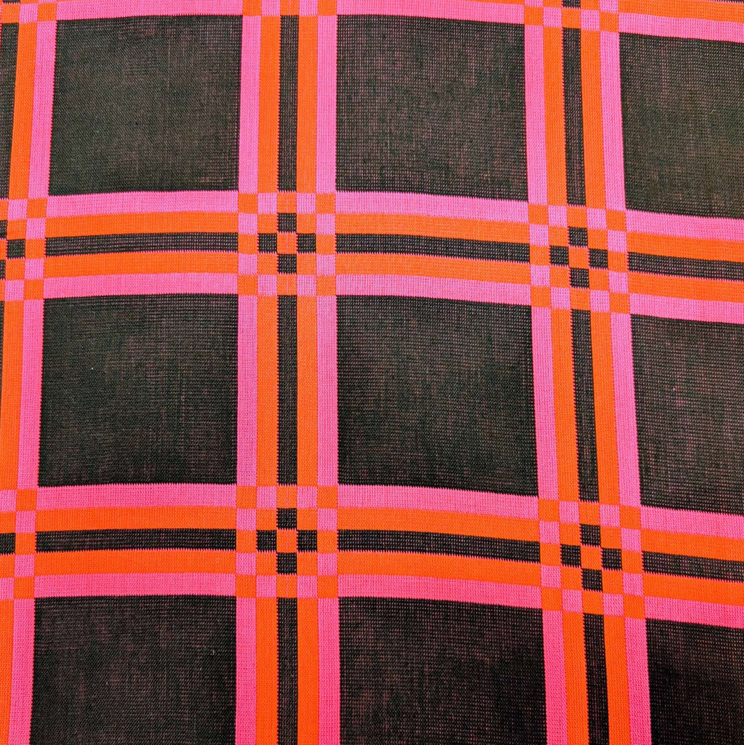 Flat lay of triple gauze Fabric with a checkered pattern of pink, orange, and black on a black background. Available at Minerva's Bower