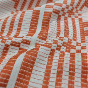 Flat lay of pure Indian cotton jacquard, Fableism Astrid Weave, in orange colourway. Available from Minerva's Bower. Fabric draped to show how it handles