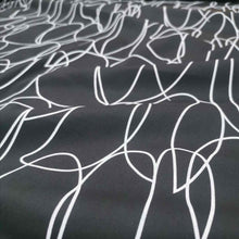 Load image into Gallery viewer, Klee is a stunning pure cotton with continuous, large scale, line drawings. White lines on a black background, available at Minerva&#39;s Bower. Fabric is draped across bench