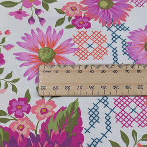 Close up of 100% cotton by moda with Colourful floral pattern with pink, purple, and green flowers on a cream background, ruler included for scale