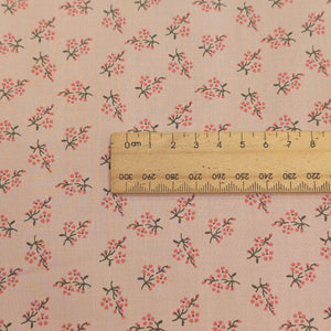 Close up of Japanese cotton fabric with a small floral pattern on a soft pink base, with ruler included for scale, for sale at Minerva's Bower