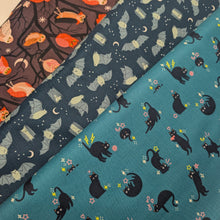 Load image into Gallery viewer, Pattern of black cats with flowers on a teal cotton Ruby Star Society fabric background. Made in Japan. Available at Minerva's Bower. Fabric draped to show how it handles. Collection of fabric bolts shown