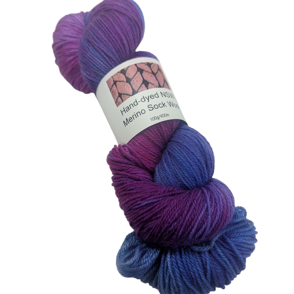 Hand-dyed merino sock yarn skein in purple and blue with a label on a white background