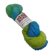 Load image into Gallery viewer, Green and Blue Multicolored merino sock yarn skein with a label on a white background
