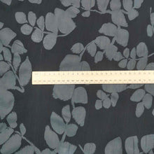 Load image into Gallery viewer, Liana is a drapey, lightweight, pure cotton voile, with the silhouette of foliage as a grey contrast on black background. Available at Minerva&#39;s Bower. Image includes a ruler for scale