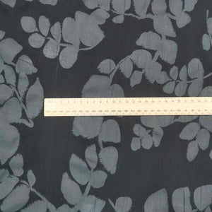 Liana is a drapey, lightweight, pure cotton voile, with the silhouette of foliage as a grey contrast on black background. Available at Minerva's Bower. Image includes a ruler for scale