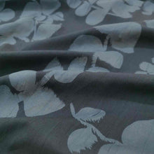 Load image into Gallery viewer, Liana is a drapey, lightweight, pure cotton voile, with the silhouette of foliage as a grey contrast on black background. Available at Minerva&#39;s Bower. Fabric is draped across bench