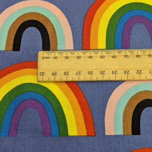 Close up of Alexander Henry cotton Fabric with rainbow pattern on a blue background, for sale at Minerva's Bower, ruler included for scale